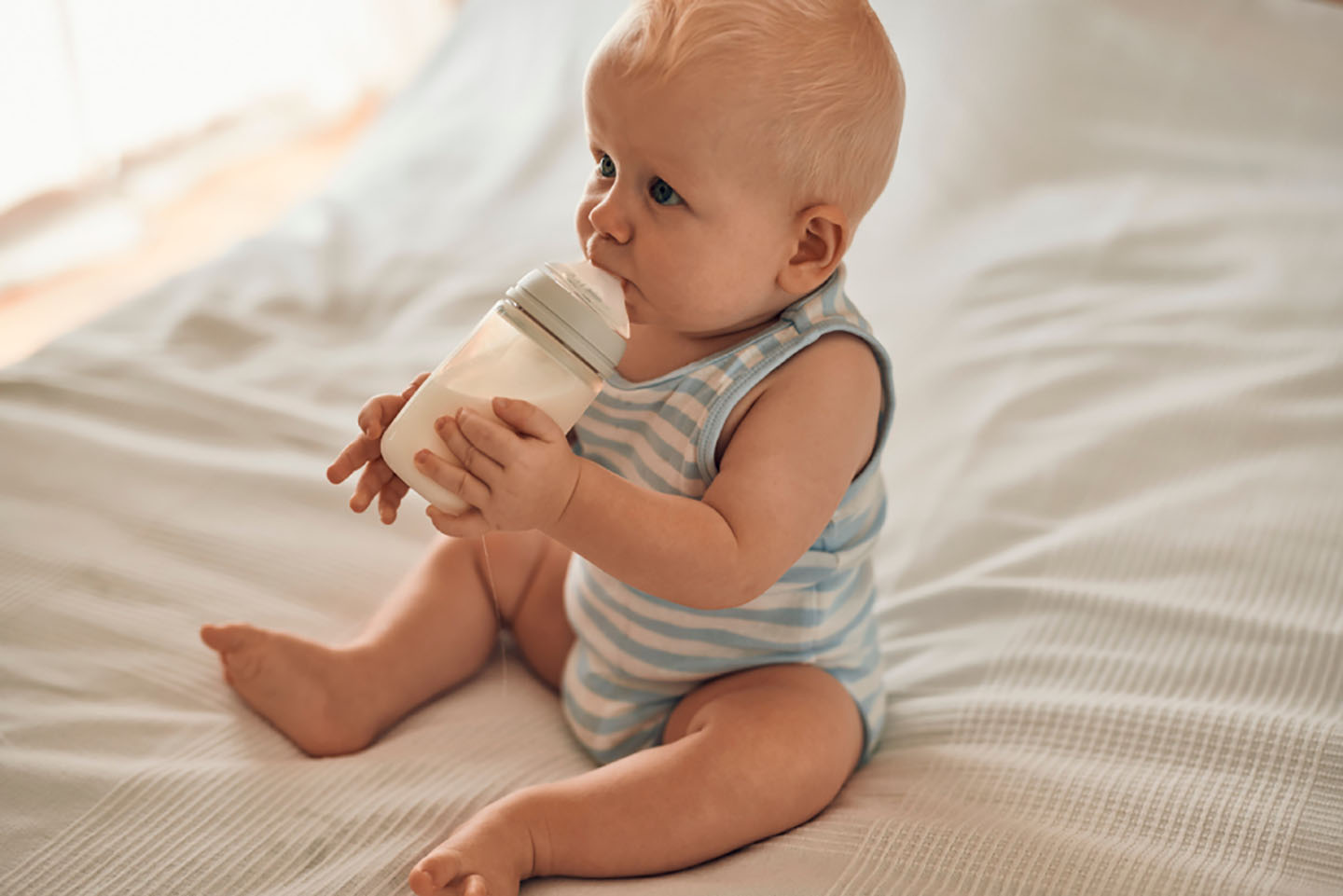 Diese Szene zeigt ein Baby, das auf dem Bett sitzt und eine Flasche in den Händen hält – ein wichtiger Schritt in Richtung selbstständigem Trinken. Das richtige Timing und die passende Menge beim Füttern aus der Flasche spielen eine große Rolle für die gesunde Entwicklung und das Wohlbefinden des Babys. Eltern können mit geeigneten Produkten und klaren Fütterungsrichtlinien sicherstellen, dass ihr Kind optimal versorgt wird.