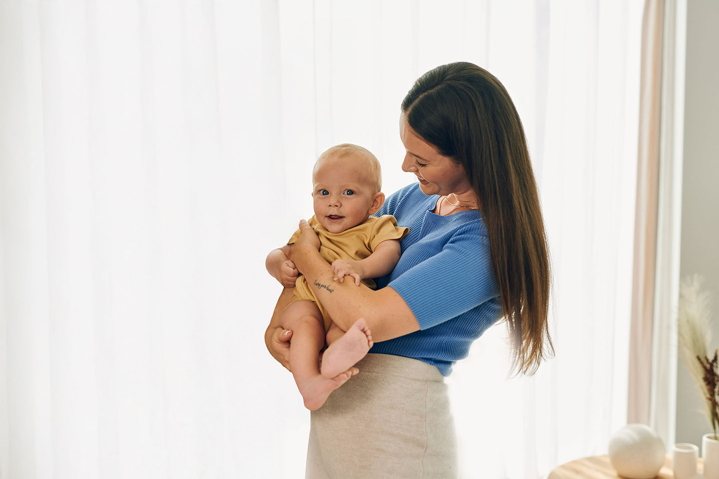 Diese Szene zeigt eine Mutter, die ihr Baby zärtlich im Arm hält und es liebevoll anschaut. Solche innigen Momente stärken die emotionale Bindung, geben dem Baby Sicherheit und schaffen eine warme, vertrauensvolle Umgebung – besonders wichtig in den ersten Lebensmonaten.