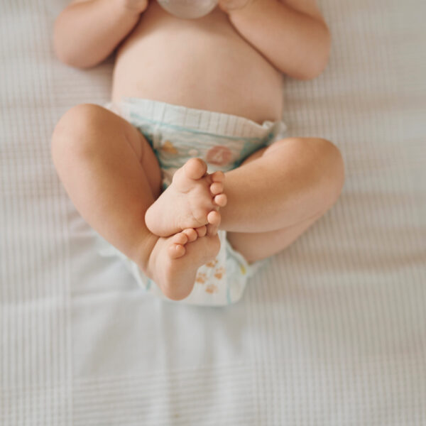 Ein Baby liegt mit angehobenen und gekreuzten Beinen, während es Unterstützung bei Verstopfung benötigt.