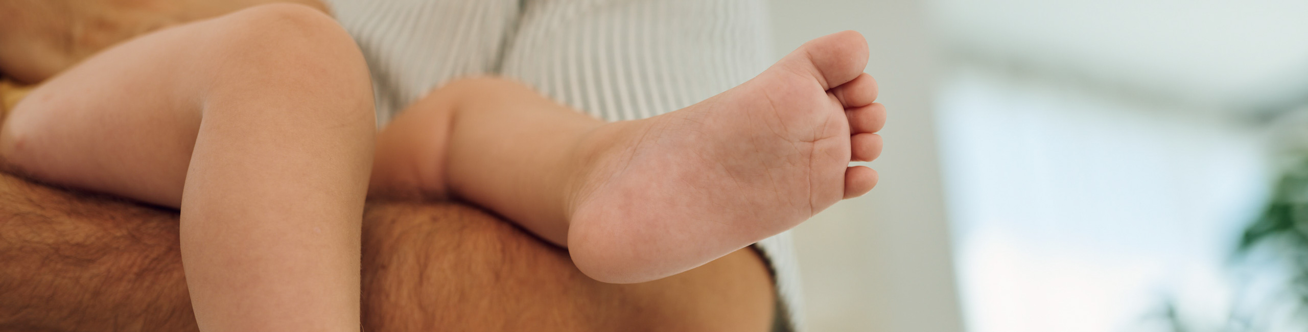 Diese Nahaufnahme zeigt die kleinen, zarten Beine und Füße eines Babys – ein Symbol für den Beginn des Lebens und die besondere Fürsorge, die Neugeborene benötigen. Solche liebevollen Details unterstreichen die Bedeutung von Geborgenheit, Nähe und einer sicheren Umgebung in den ersten Lebensmonaten.