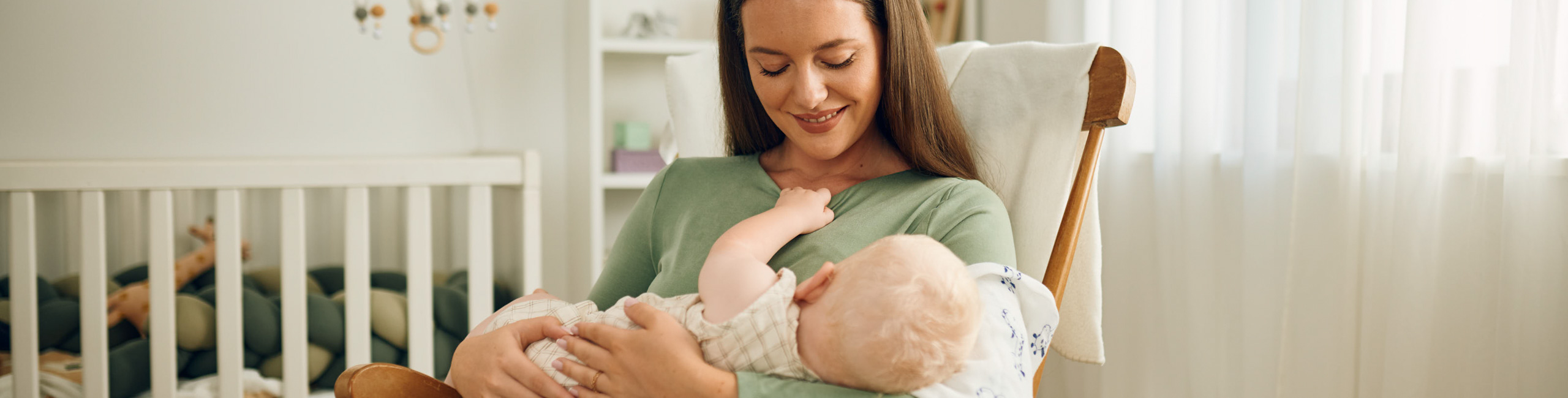 Diese Szene zeigt eine Mutter, die in einer Hängeschaukel sitzt und ihr Baby liebevoll im Arm stillt. Die ruhige Umgebung schafft Geborgenheit und fördert die enge Bindung zwischen Mutter und Kind. Stillen unterstützt die gesunde Entwicklung des Babys und bietet Schutz durch wichtige Nährstoffe und Antikörper.