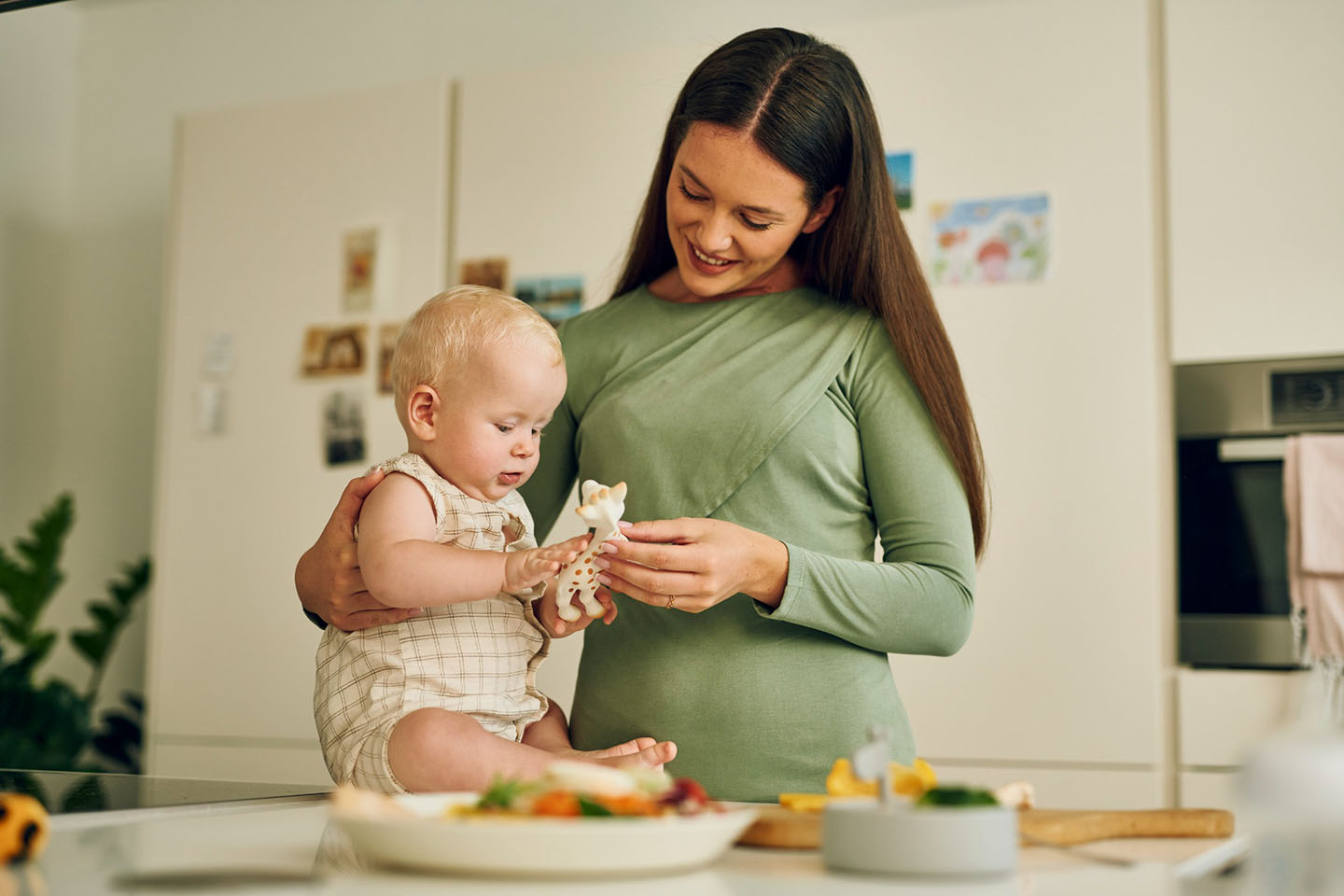Diese Szene zeigt eine Mutter und ihr Baby, die zusammen am Tisch sitzen und eine Mahlzeit teilen. Die Einführung erster einfacher Beikost ist ein wichtiger Entwicklungsschritt für das Baby. Eine ruhige, positive Essenssituation unterstützt das Lernen neuer Geschmäcker und fördert gesunde Ernährungsgewohnheiten von Anfang an.