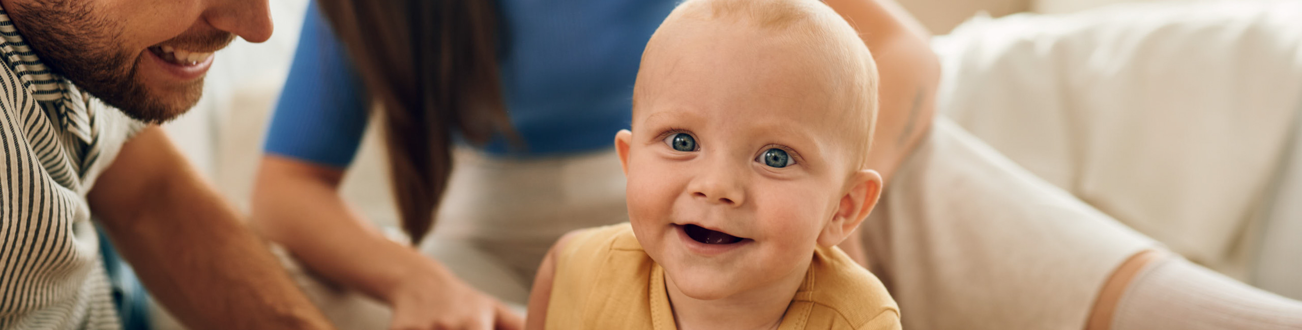 Diese Szene zeigt eine glückliche junge Familie, bestehend aus Vater, Mutter und ihrem Baby. Solche gemeinsamen Augenblicke stärken die familiäre Bindung und schaffen eine liebevolle, sichere Umgebung, die für die Entwicklung des Babys besonders wichtig ist.