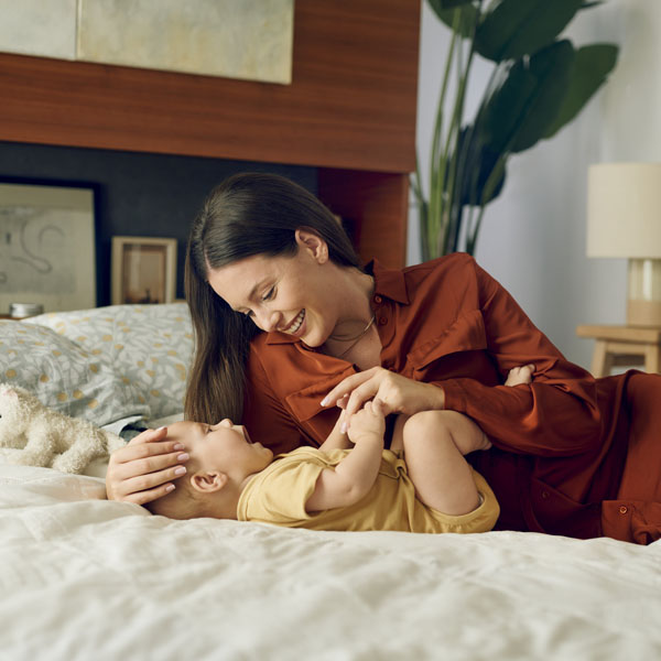 Diese Szene zeigt eine Mutter und ihr Baby, die sich auf dem Bett liebevoll ansehen – ein wertvoller Moment voller Nähe und spielerischem Lernen. Solche Situationen fördern die emotionale Bindung, unterstützen die frühe Entwicklung und schaffen eine warme, sichere Umgebung, in der das Baby neugierig die Welt entdeckt.