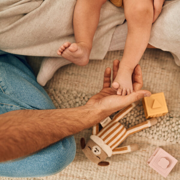 Diese Szene zeigt einen Vater, der sanft den Fuß seines Babys hält, während das Neugeborene auf einem weichen Teppich mit Spielzeug liegt. Solche ruhigen, liebevollen Augenblicke stärken die Bindung und vermitteln dem Baby ein Gefühl von Sicherheit und Geborgenheit in seinen ersten Tagen zu Hause.