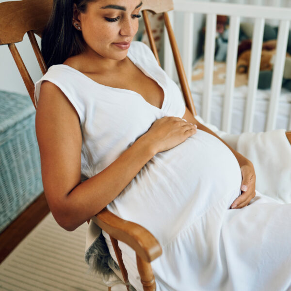 Diese Szene zeigt eine schwangere Frau, die ruhig im Schaukelstuhl sitzt – ein Symbol für Achtsamkeit und Fürsorge während der Schwangerschaft. Die Darstellung verweist auf die Bedeutung von Folsäure in der frühen Schwangerschaft, um Neuralrohrdefekte vorzubeugen. Eine gute Versorgung mit aktiver Folsäure wie Quatrefolic® spielt eine entscheidende Rolle für die gesunde Entwicklung des Babys.