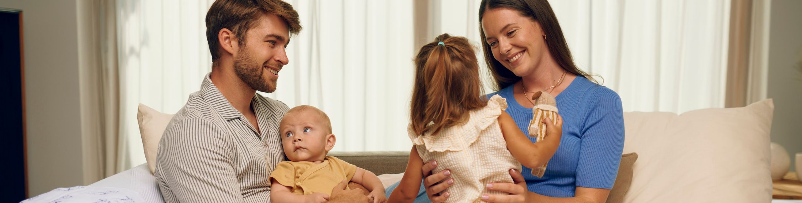 Obitelj sjedi na kauču, roditelji, beba i jednogodišnja kćer