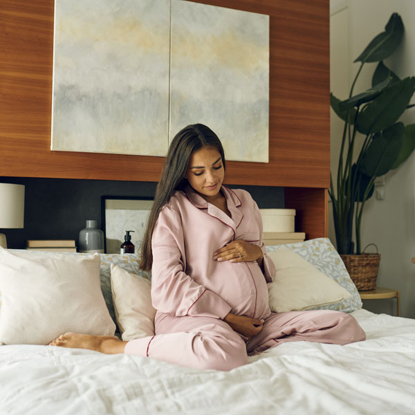 Diese Szene zeigt eine schwangere Frau in einem rosa Bademantel, die die Packung von Novalac Prenatal mit der aktiven Folsäureform Quatrefolic hält. Novalac Prenatal versorgt werdende Mütter gezielt mit wichtigen Nährstoffen wie Folsäure, Eisen und DHA, die für eine gesunde Schwangerschaft entscheidend sind. Die aktive Form Quatrefolic ist besonders gut verfügbar und unterstützt die optimale Entwicklung des Babys schon ab der frühen Schwangerschaftsphase.