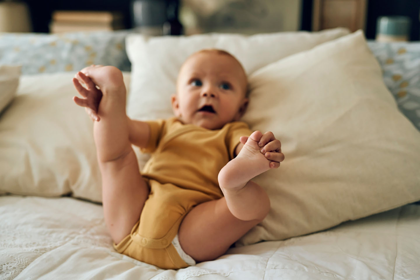 Ein glückliches Baby liegt auf dem Bett und lächelt – unterstützt von Novalac.