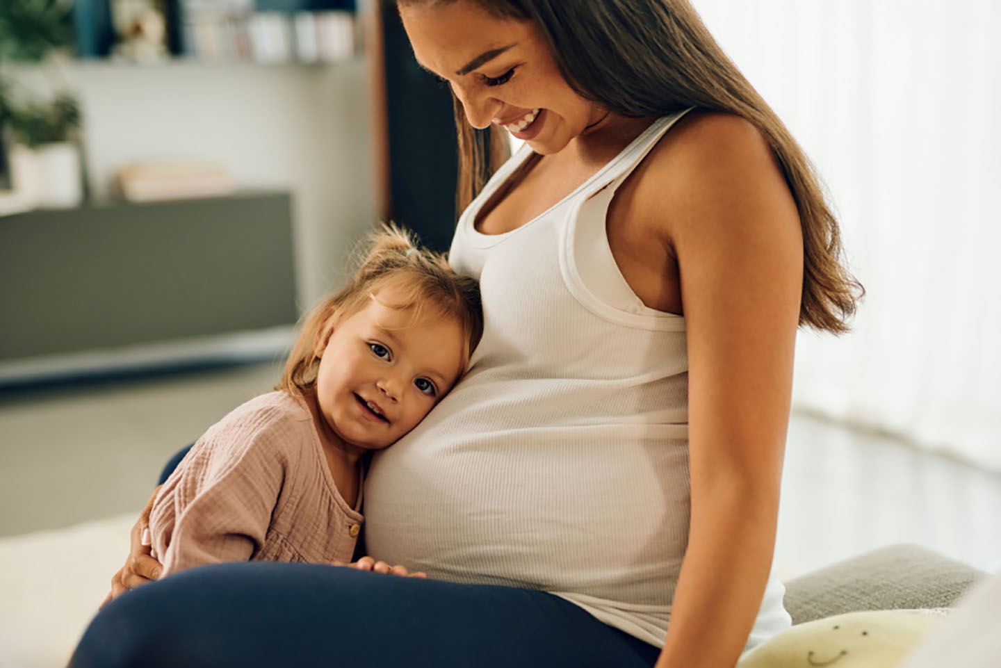 Diese Szene zeigt ein Kleinkind, das den Bauch seiner schwangeren Mutter umarmt – ein zärtlicher Moment, der Vorfreude, Geborgenheit und familiäre Verbundenheit ausdrückt. Solche Augenblicke stärken die emotionale Bindung innerhalb der Familie und helfen dem Kind, sich auf das neue Geschwisterchen vorzubereiten.