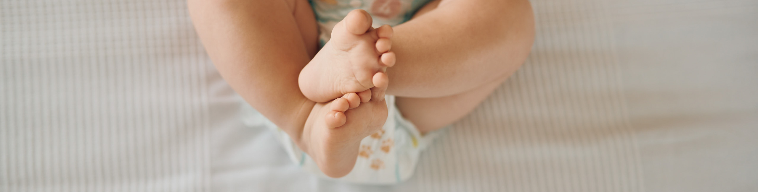 Diese Szene zeigt ein Baby, das aufgrund von Verstopfung auf dem Bett liegt und seine Beine gekreuzt hält – eine typische Haltung bei Bauchbeschwerden. Verstopfung ist bei Säuglingen häufig und kann zu Unruhe und Unwohlsein führen. Die richtige Ernährung und sanfte Unterstützung helfen, die Verdauung zu regulieren und das Wohlbefinden des Babys zu verbessern.